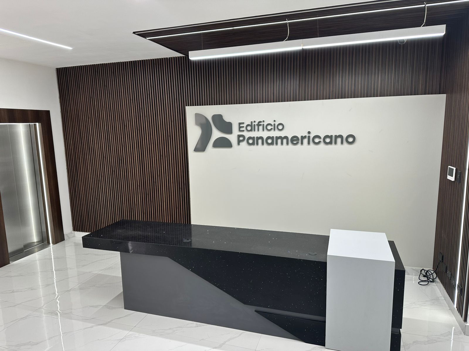 Lobby terminado Edificio Panamericano — recepción con mármol, logo iluminado y ascensores premium